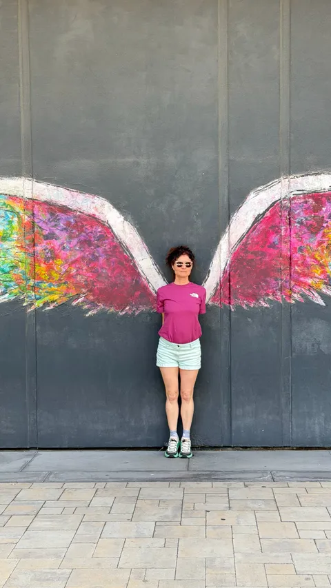 Fit et Kiff devant une fresque murale, des ailes colorées peintes de chaque côté